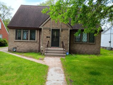 A small brick house with a front porch and green lawn.
