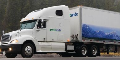 A white semi-truck with a trailer featuring a mountain landscape graphic.
