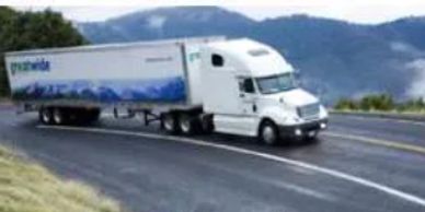 White semi-truck with trailer driving on a curved mountain road.