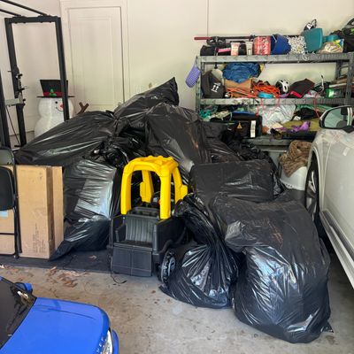 Garage cluttered with black trash bags, toys, and car.