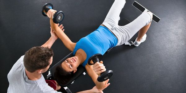 A Personal trainer assisting client with weights.