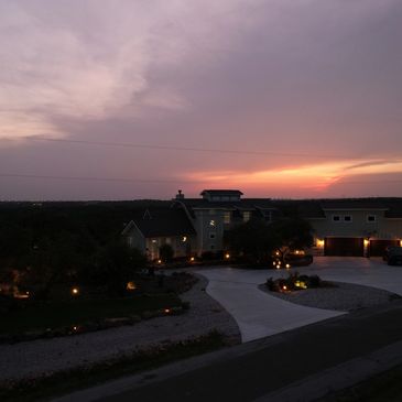 A house with illuminated garden lights at sunset under a cloudy sky.