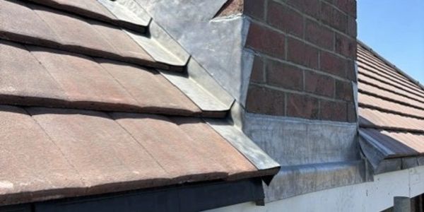 Close-up of a tiled roof with brick chimney and metal flashing.