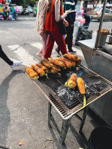 Traditional Mexican street corn cooking on the side of the road in Mexico City while people walk by