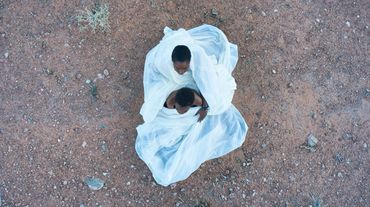 Aerial view from drone photo of Desert Queen and son seated on ground wrapped in fabric.