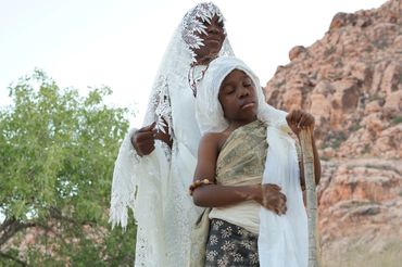 Desert Queen with White laced attire with hand on son’s shoulder.