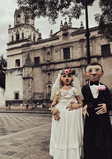 Giant sized bride and groom puppets in front of Parroquia de San Juan Bautista in Mexico City