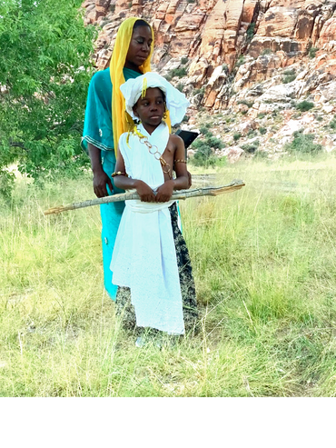 Desert Queen and Prince holding staff in open field.