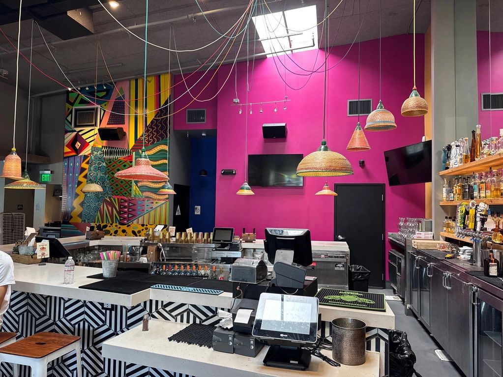 Colorful bar interior with geometric wall art and hanging lamps.