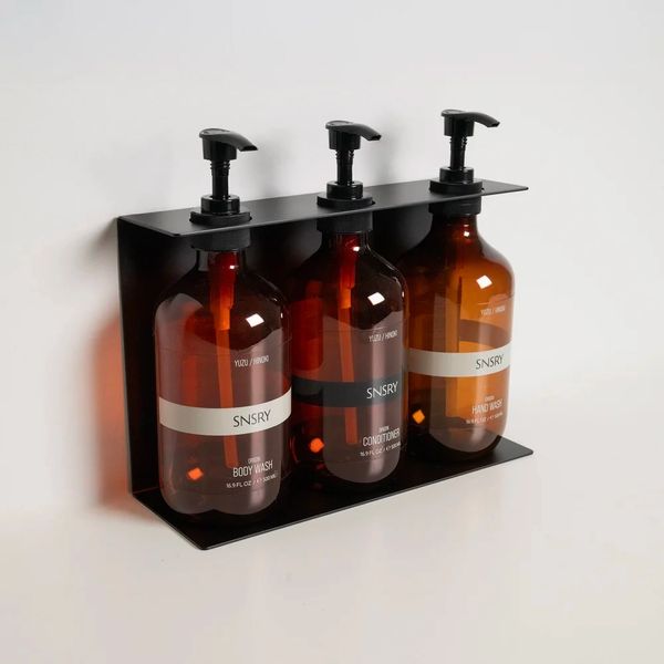 Three amber bottles with pumps on a black wall-mounted shelf.