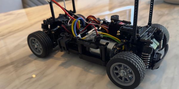 Close-up of a remote control car chassis with exposed wiring and components on a marble surface.