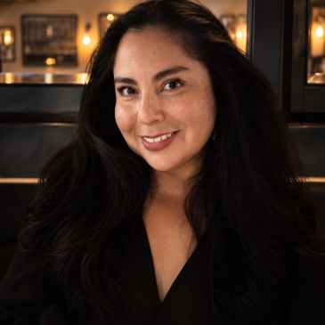 Smiling woman with long dark hair in a cozy indoor setting.