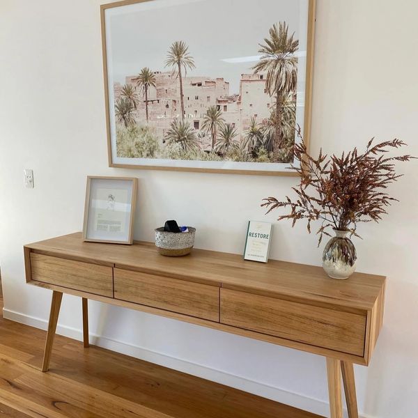 Minimalist wooden console table with framed art and dried floral arrangement.