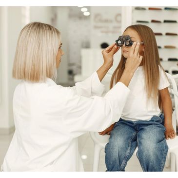 Optometrist fitting a young girl with trial frames for an eye exam.
