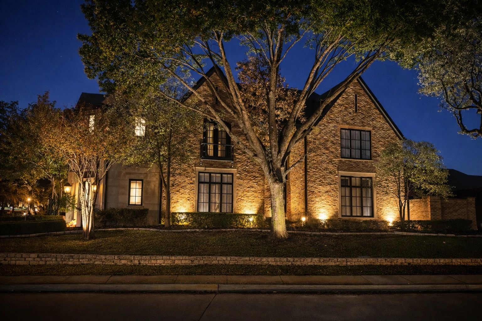 A warmly lit brick house at night surrounded by trees.