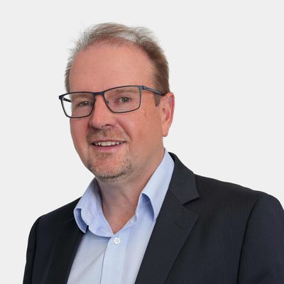 Man in glasses and suit smiling against plain background.