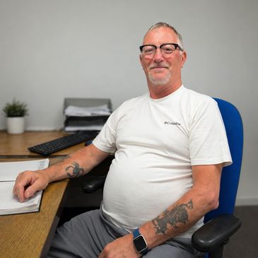 Smiling man with tattoos sitting at a desk in an office setting.