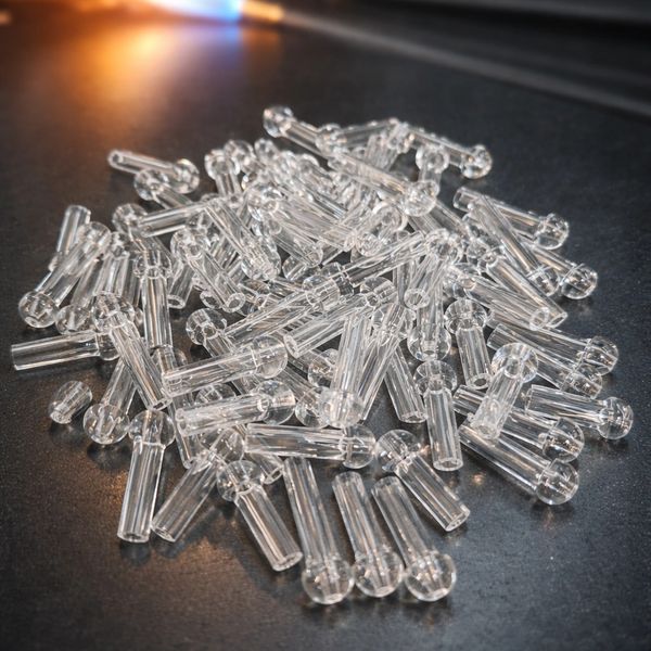 A pile of clear plastic or glass small cylindrical rods on a dark surface.
