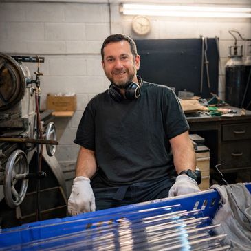 Smiling man in a workshop with gloves and headphones around his neck.