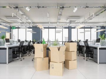 Stack of moving boxes in a modern office space with empty desks.