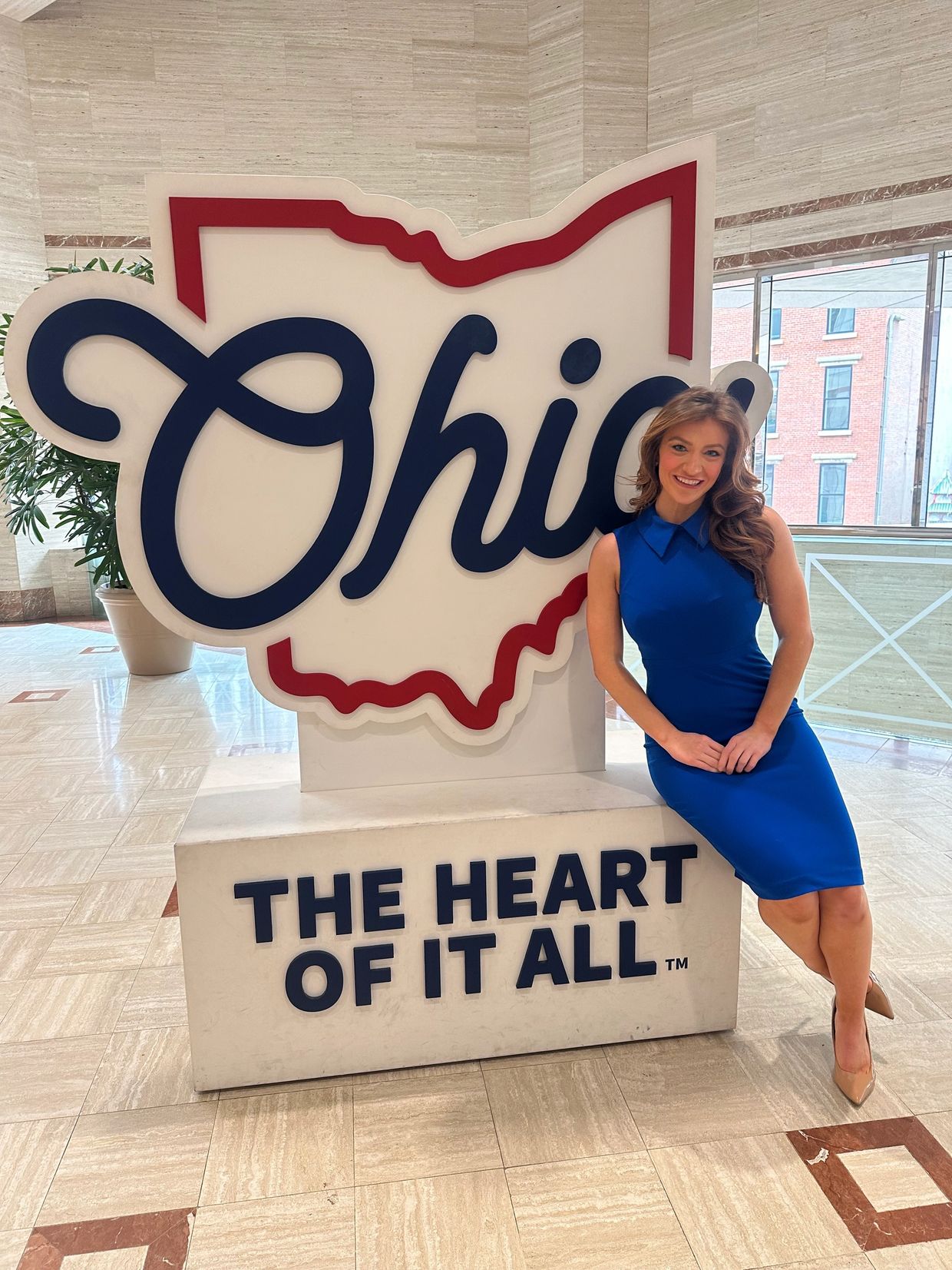 A woman in a blue dress sitting by an Ohio state sign indoors.