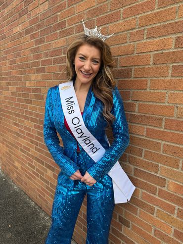Woman wearing a blue sequined outfit and Miss Clayland sash with a crown.