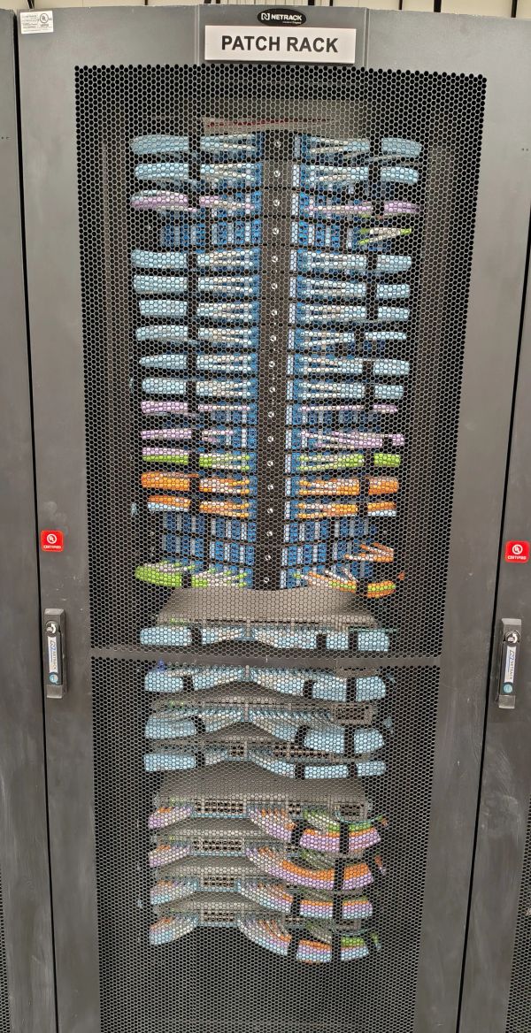 Network patch rack with organized cables behind mesh door.