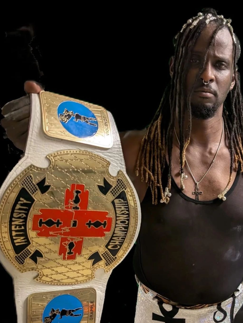 Man with dreadlocks holds up an Intensity Championship wrestling belt.
