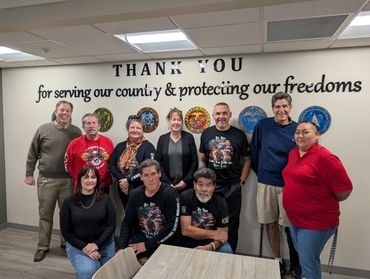 Group photo of diverse people in front of a military appreciation wall.