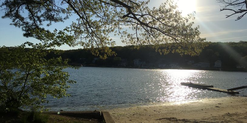Sunlight reflecting on a calm lake with trees and a dock.