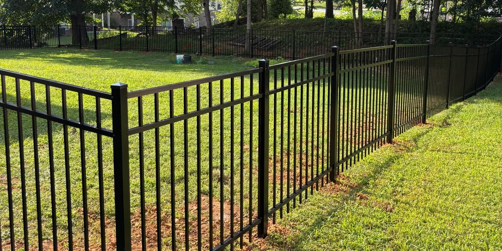 A black metal fence encloses a grassy area with trees. Fencing Services in Kingsport