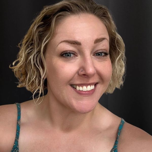 Smiling woman with short curly hair and nose piercing.