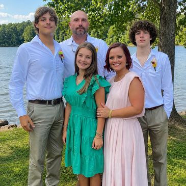 Family posing by a lake on a sunny day.