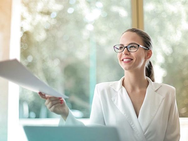 Smiling professional woman handing over a document in a bright office.
