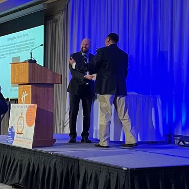 Two men exchanging an award on stage at a formal event.