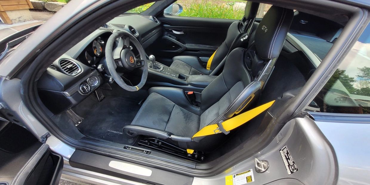 Interior of a Porsche GT4 with black seats and yellow seat belts.