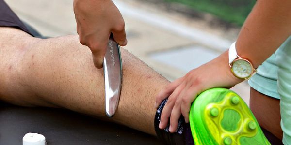 Person shaving another person's leg outdoors.