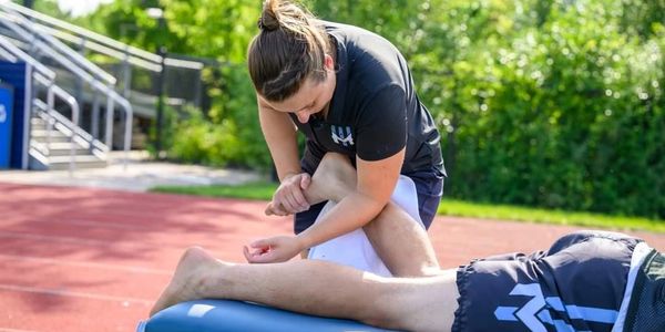 Physical therapist stretching a patient's leg outdoors.