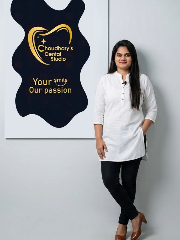 A woman stands confidently beside a dental studio sign.
