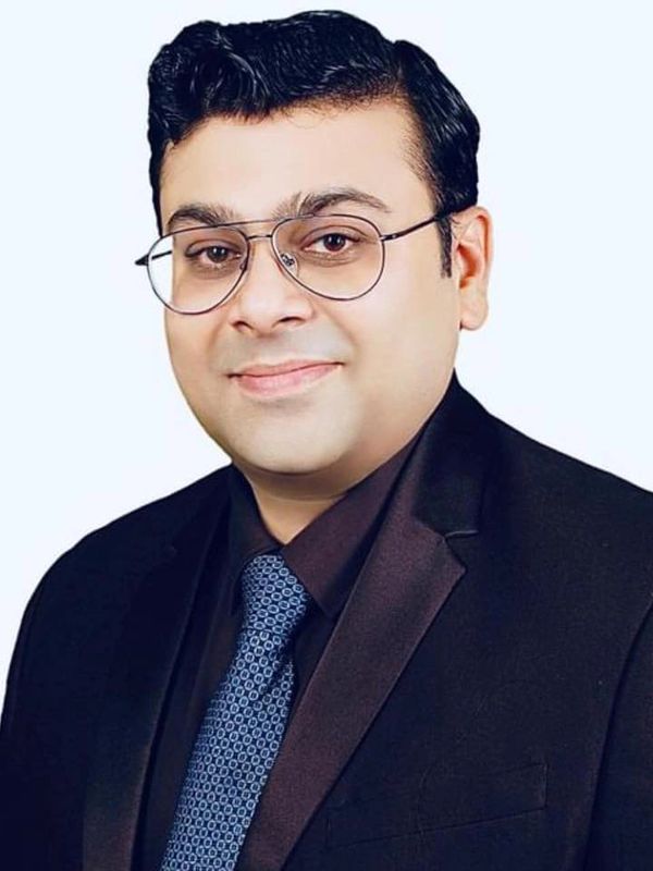 Portrait of a man in a black suit and patterned blue tie with glasses.