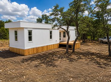 A modern white tiny house on a wooden foundation surrounded by trees.