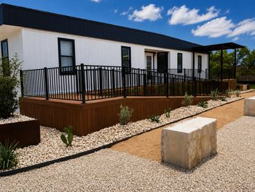 Modern white house with black trim and a wooden ramp under a blue sky.
