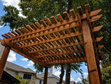 Wooden pergola structure in a backyard with trees and houses in the background.