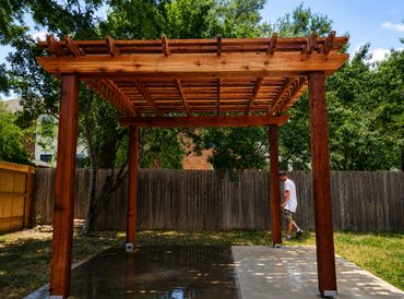 Wooden pergola in a backyard with a person walking nearby.
