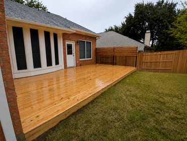 Newly built wooden deck attached to a brick house with a fenced backyard.