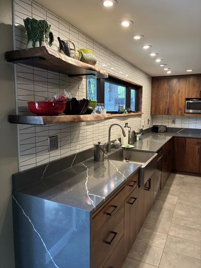 Modern kitchen with dark wood cabinets, marble countertops, and open shelving.