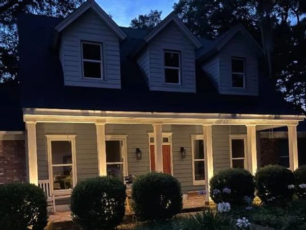 landscape lights behind bushes light up the front columns of a house.