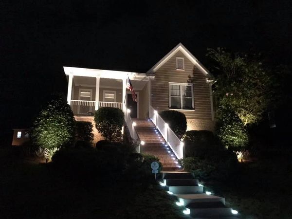 Stair lights are placed along a long stairway leading up to a house. The house also is illuminated.