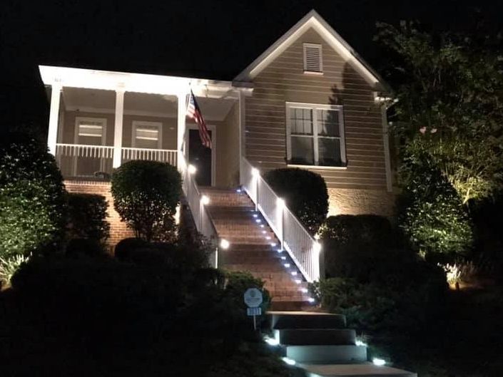 House with cozy lighting. Outdoor walkway lighting, stair lighting, flood lights on landscaping.