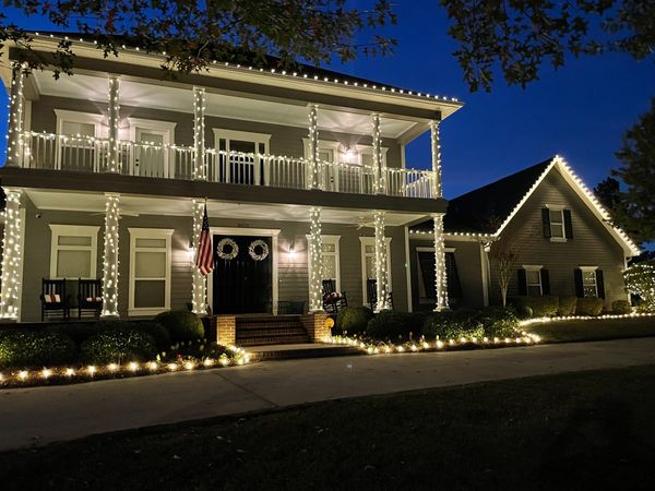 White Christmas lights decorating a two-story home, wrapped around columns on both levels.